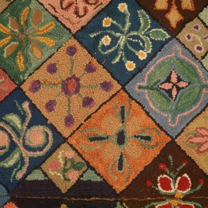 Detailed view of a brightly colored, chunky hooked rug with floral patchwork on light wood planks.