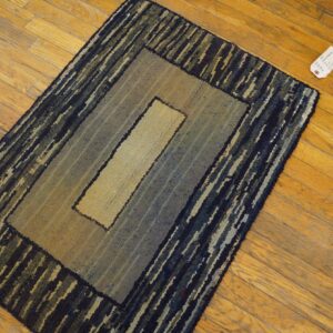 Textured rug with concentric borders in tan, muted blue, and dark stripes on a hardwood floor.