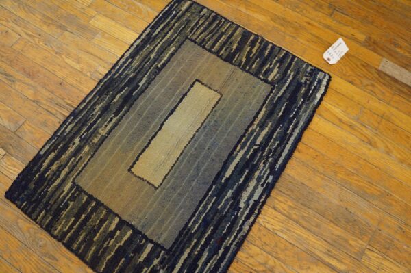 Textured rug with concentric borders in tan, muted blue, and dark stripes on a hardwood floor.