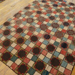 Multicolored diamond grid rug with dark circular motifs rests on a rustic yellow wood plank floor.