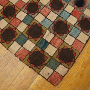 Geometric high-pile rug in brown, red, teal, and cream diamonds rests on worn wooden planks.