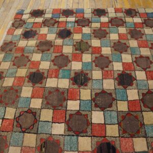 A textured low pile rug featuring a multi-color checkerboard pattern with dark star medallions, lying on wood floors.