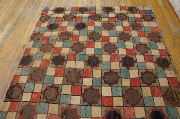 A textured low pile rug featuring a multi-color checkerboard pattern with dark star medallions, lying on wood floors.
