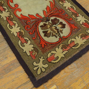A hooked rug in olive green, red, and khaki floral motifs rests on wide plank light wood flooring.