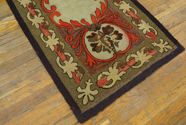 A hooked rug in olive green, red, and khaki floral motifs rests on wide plank light wood flooring.
