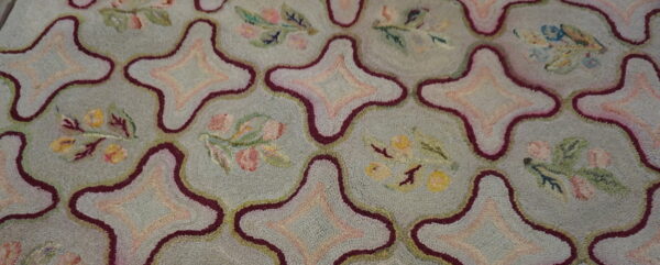 Textured rug featuring a blue-gray field, geometric maroon outlines, and pastel pink and yellow floral sprigs.