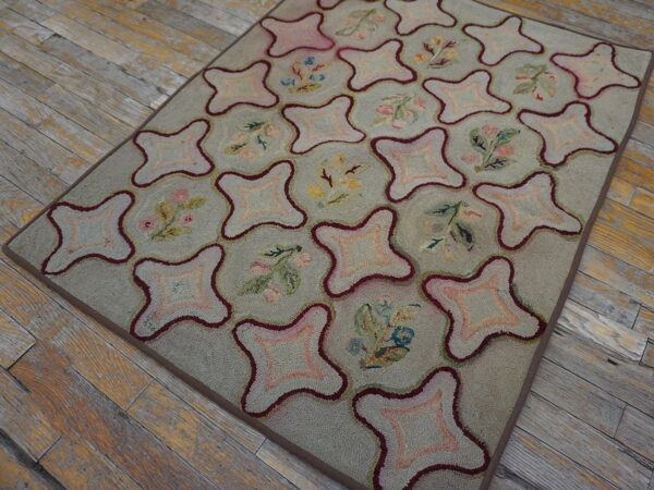 Gray-green rug with a looped texture features a burgundy geometric lattice alternating with floral and pink motifs on rustic wood floors.