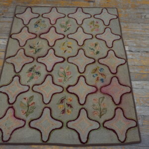 Green hooked rug featuring star medallions and floral sprigs rests on distressed wood flooring.