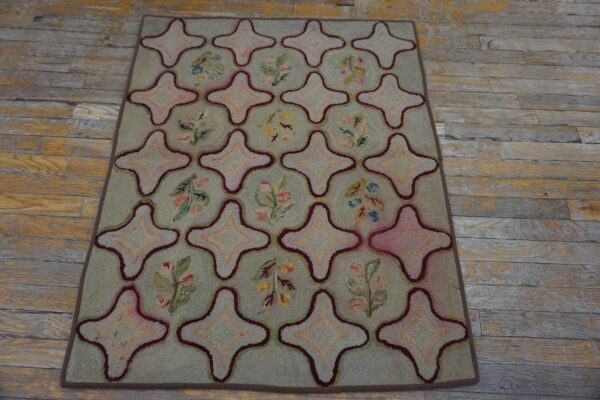 Green hooked rug featuring star medallions and floral sprigs rests on distressed wood flooring.