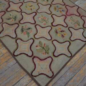 Light green hooked rug with pink and burgundy quatrefoil geometric and floral designs on wood flooring.