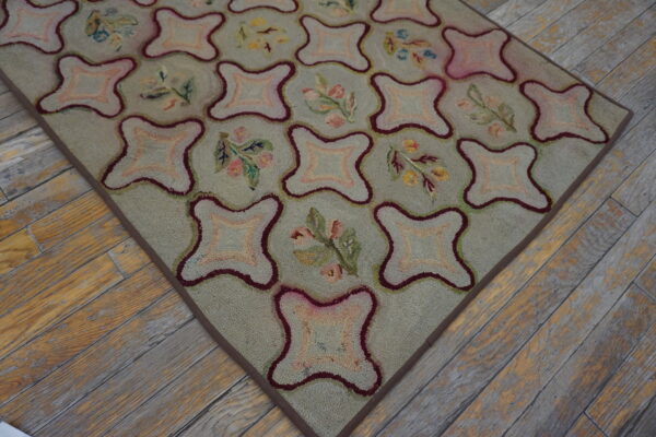 Light green hooked rug with pink and burgundy quatrefoil geometric and floral designs on wood flooring.