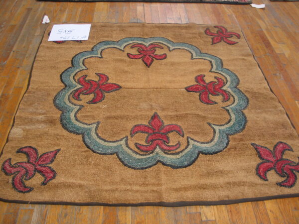Square tan rug with low, chunky texture, featuring red and teal curvilinear floral designs on wood flooring.