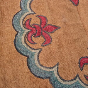 Scalloped blue and red floral motif on a textured tan rug, viewed close up on a wooden floor.