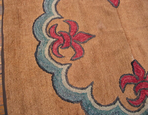 Scalloped blue and red floral motif on a textured tan rug, viewed close up on a wooden floor.