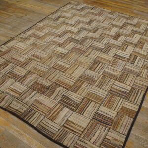 Neutral striped rag rug featuring a rectangular patchwork pattern rests on distressed wooden floorboards.