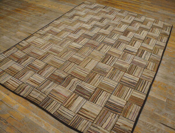 Neutral striped rag rug featuring a rectangular patchwork pattern rests on distressed wooden floorboards.