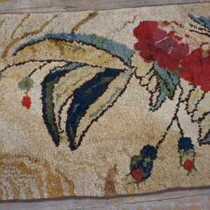 Textured beige rug featuring a large red and blue floral design over distressed wooden flooring.