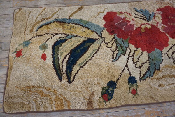 Textured beige rug featuring a large red and blue floral design over distressed wooden flooring.