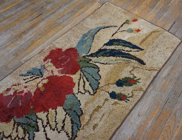 A high-pile rug featuring red flowers and teal leaves on a cream background rests on distressed wood planks.