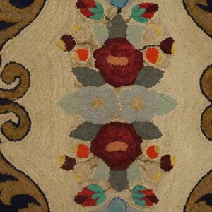 Looped rug detail with maroon floral medallions on beige, framed by brown scrolls and visible wood floor.
