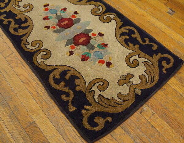 High-pile rug featuring a cream central floral panel bordered by dark blue and tan baroque scrolls on wood floors.