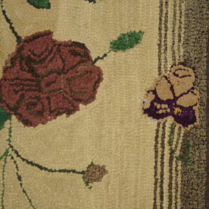 Pebbled tan rug texture with a large maroon floral design and striped dark brown border detail.