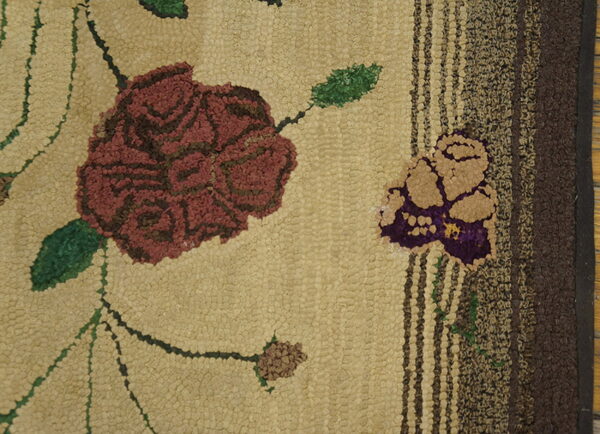 Pebbled tan rug texture with a large maroon floral design and striped dark brown border detail.