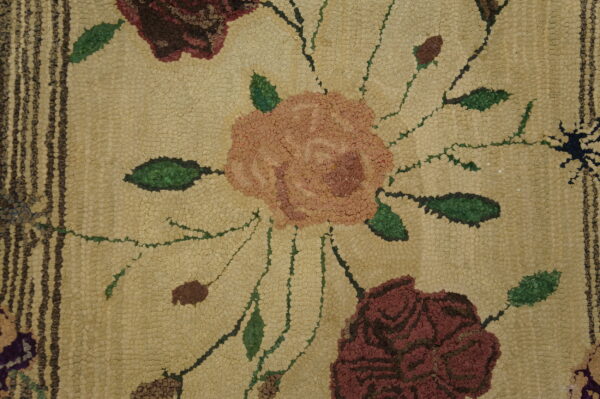 Bumpy texture of a hooked rug featuring pink and deep red roses on a tan field with green stems.