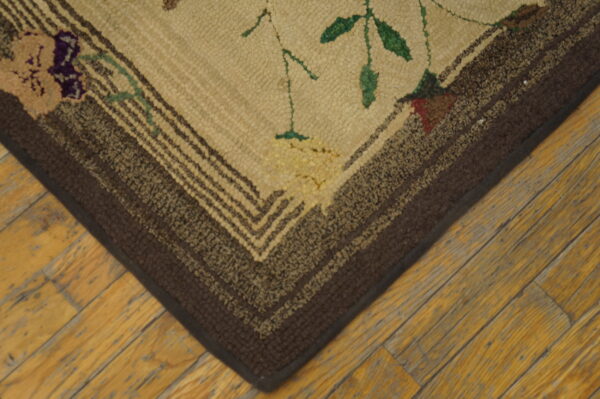 Textured beige rug corner displays floral patterns, brown striped borders, and sits on yellow plank hardwood flooring.