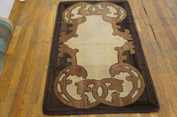 Ornate dark brown and tan scroll runner rug on worn light brown plank hardwood flooring.