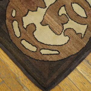 Loop pile rug in brown and tan scroll pattern rests on light-colored plank hardwood flooring.