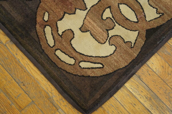 Loop pile rug in brown and tan scroll pattern rests on light-colored plank hardwood flooring.