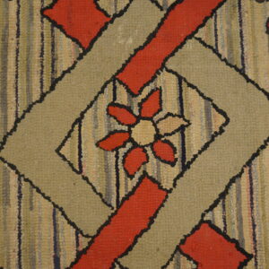 Textured hooked rug with a beige and red floral design inside a black-outlined geometric diamond shape.