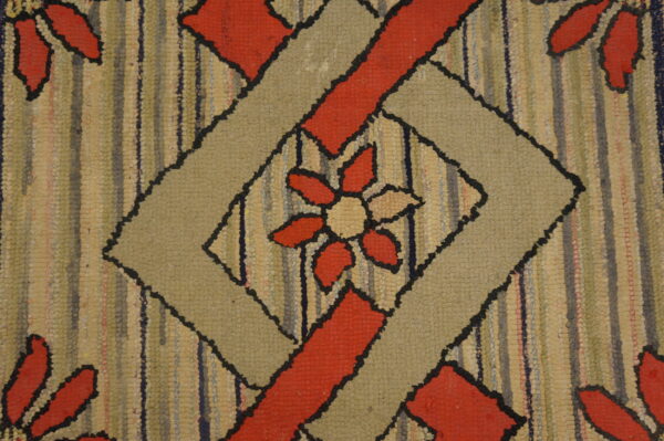 Textured hooked rug with a beige and red floral design inside a black-outlined geometric diamond shape.