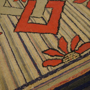 Striped textured rug with large red floral and geometric motifs, shown angled against light wood flooring.