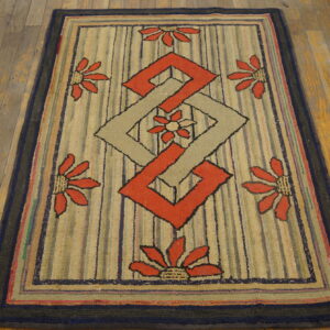 Low-pile rug with geometric and floral patterns in red and tan on a striped field over wood flooring.