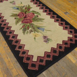Beige rug with multicolored flowers, a maroon and black geometric border, sits on rustic wood.