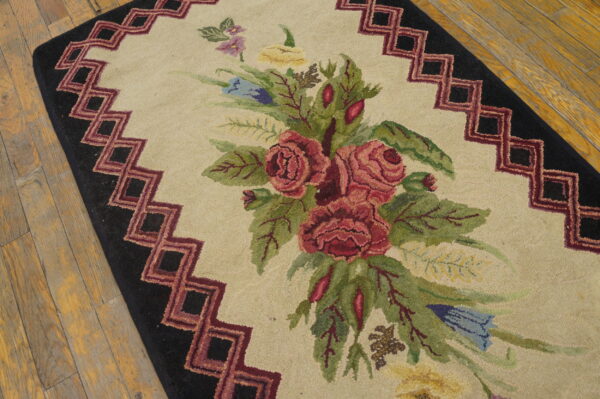 Beige hooked rug with red, green, and blue floral design and black stepped geometric border on wood floor.