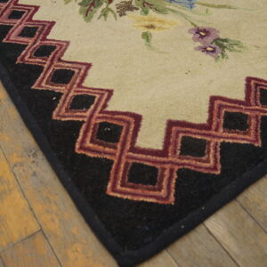 Floral and geometric rug corner in cream, black, and red, resting on distressed light wood planks.