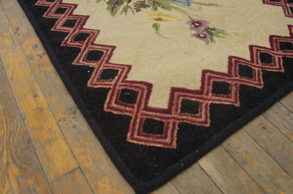 Floral and geometric rug corner in cream, black, and red, resting on distressed light wood planks.
