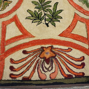 Hooked rug detail showing beige, vibrant orange, and green floral motifs on rough wood planks.