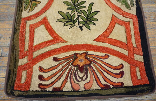 Hooked rug detail showing beige, vibrant orange, and green floral motifs on rough wood planks.