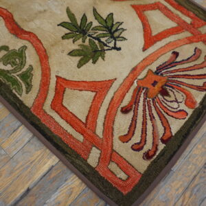 Beige hooked rug with interlocking orange, green, and red floral designs on weathered wood floor.