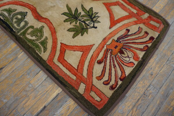 Beige hooked rug with interlocking orange, green, and red floral designs on weathered wood floor.