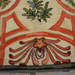 Cream and orange high-texture hooked rug with stylized floral design resting on distressed wood floors.