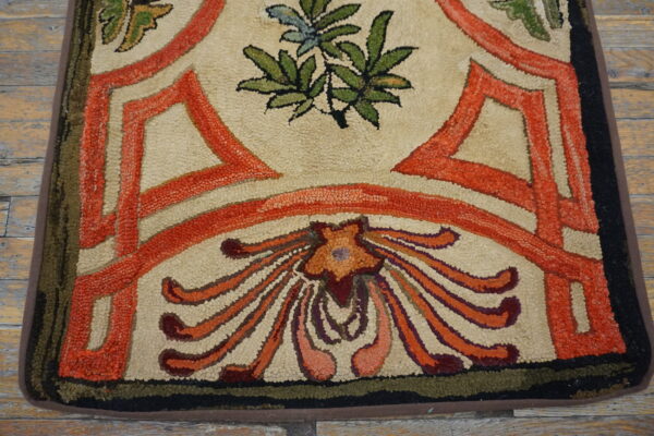 Cream and orange high-texture hooked rug with stylized floral design resting on distressed wood floors.