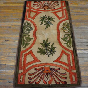Beige runner with bold orange borders and green floral motifs on distressed wood flooring.