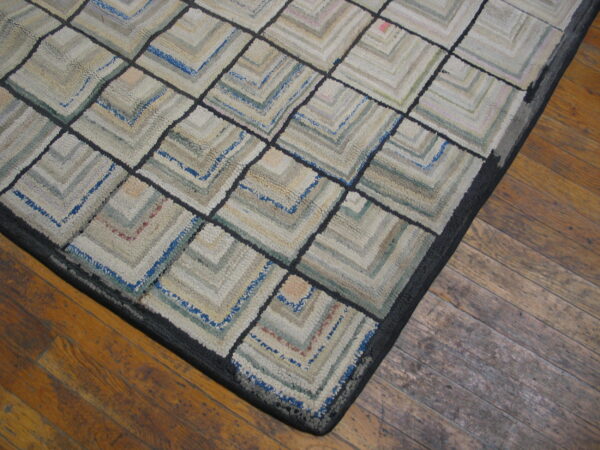 Chunky textured rug featuring a muted neutral and blue concentric square pattern rests on a distressed wood floor.