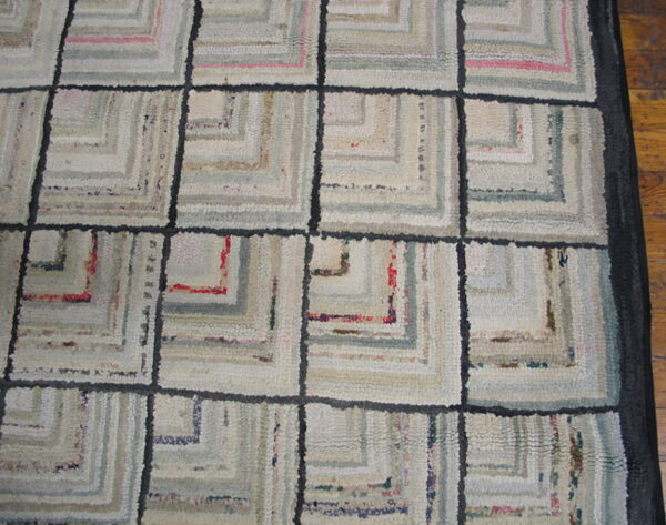 A pale log cabin grid rug with light gray, cream, and pink concentric squares on a wood floor.