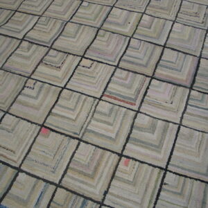 Textured gray and cream rug featuring a dark grid over geometric concentric square patterns on wood flooring.